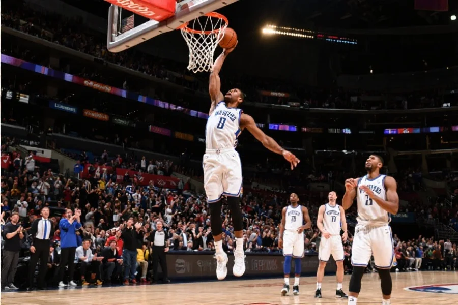 NBA决赛现场特写，一位球员高高跃起正准备扣篮，背景为欢呼的球迷和队友